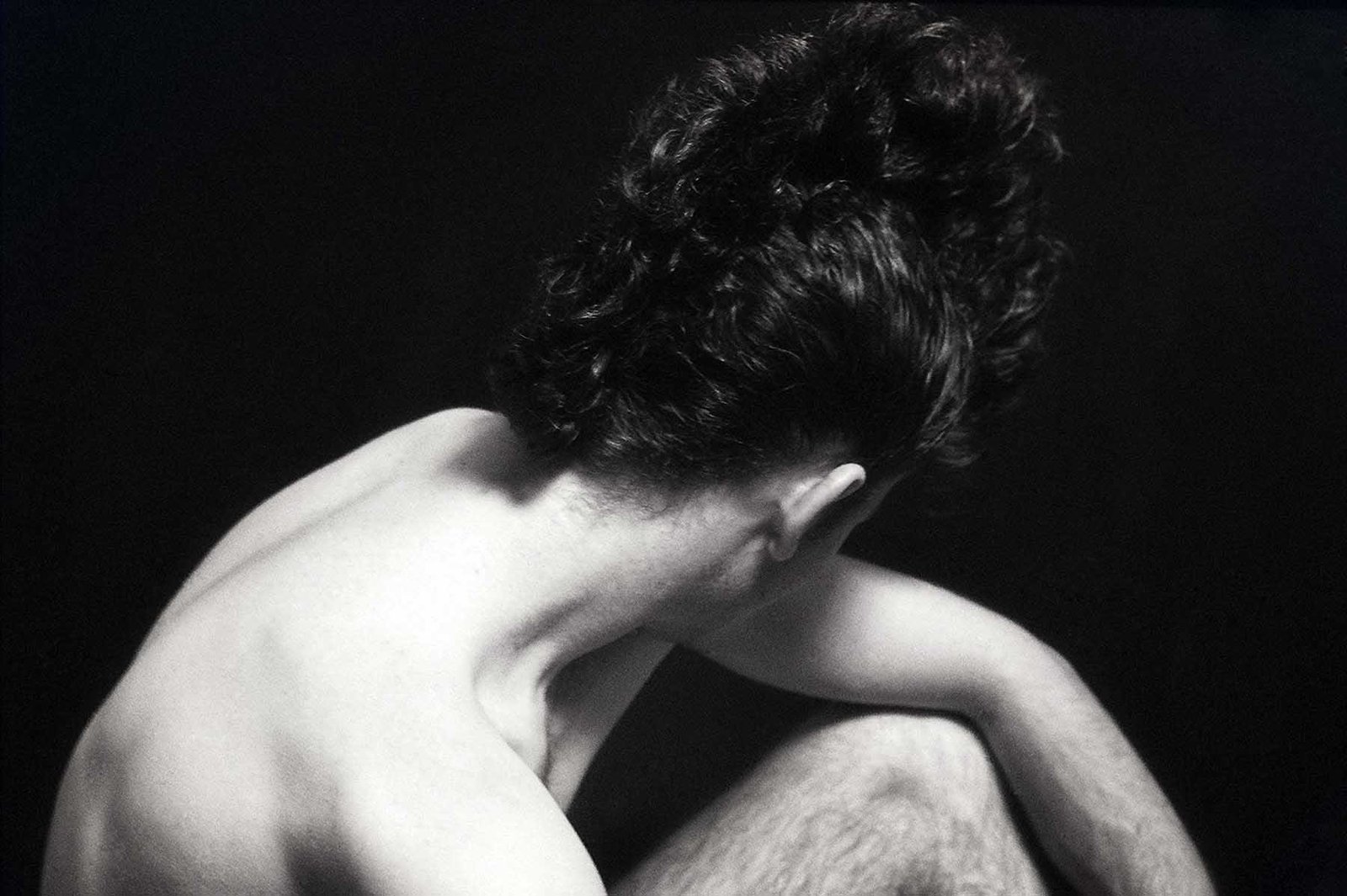 Black-and-white fine art portrait by Milan Stamenovic depicting a seated male figure in a withdrawn posture, exploring bodily resonance, inner rhythm, and the emergence of sonic identity before articulation.