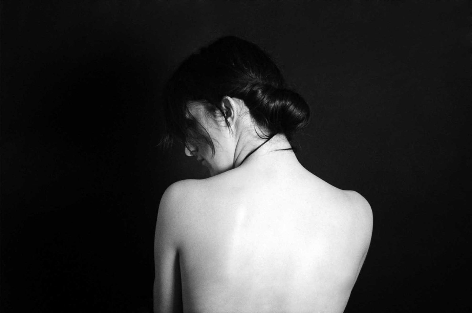 Black-and-white fine art portrait by Milan Stamenovic depicting the bare back of a woman turned away from the camera, conveying introspection, vulnerability, and silent emotional intensity.