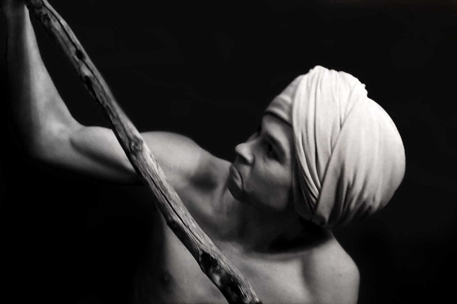 Black-and-white fine art analog portrait of a human figure extending an arm while holding a staff, suggesting gesture, direction, and emergence within a myth-inspired photographic study by Milan Stamenovic.