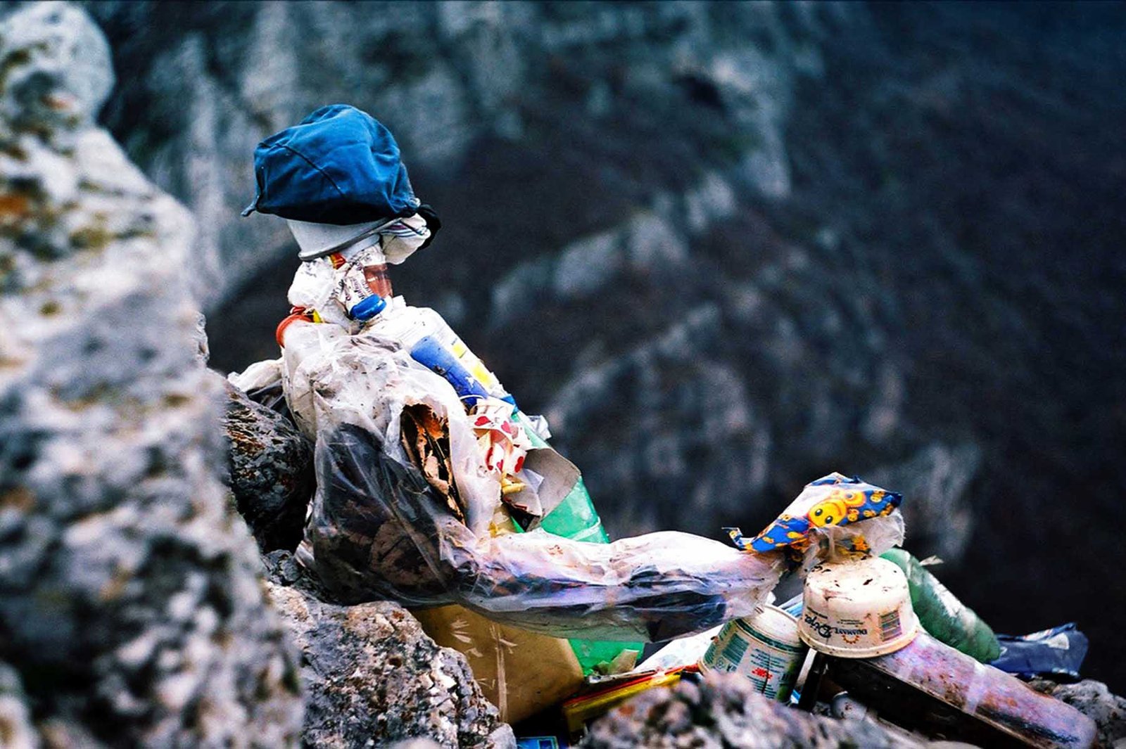 Fine art analog photograph depicting a human-like figure composed of discarded materials positioned within a rocky landscape, exploring human dominance, waste, and ecological consequence in a photographic work by Milan Stamenovic.