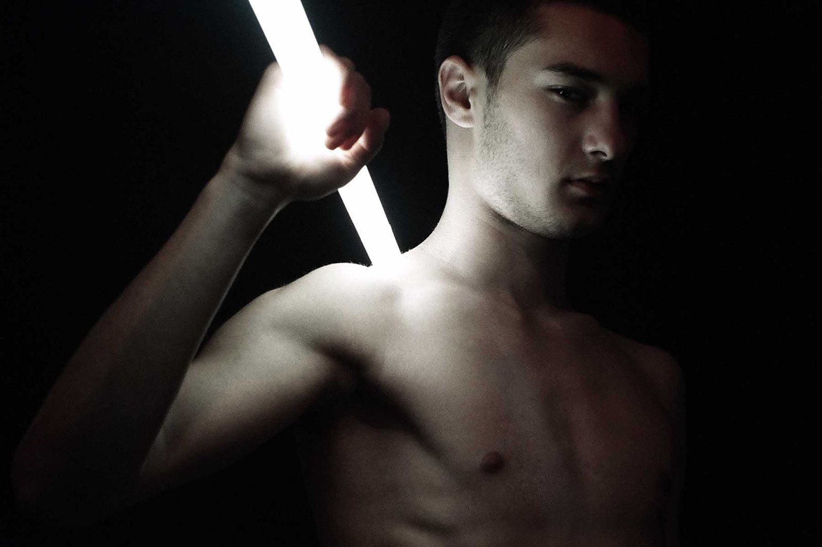Portrait photograph examining the physical consequence of artificial illumination on the human body, isolating light as an active force rather than a neutral source.