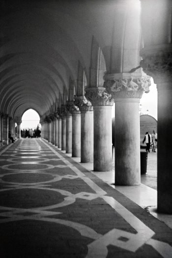 Arched stone corridor with receding columns photographed on analog film by Milan Stamenovic, exploring absence, passage, and irreversible movement through architectural space in Landscapes of the Remembering World.