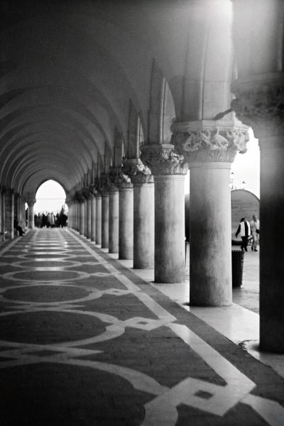 Arched stone corridor with receding columns photographed on analog film by Milan Stamenovic, exploring absence, passage, and irreversible movement through architectural space in Landscapes of the Remembering World.