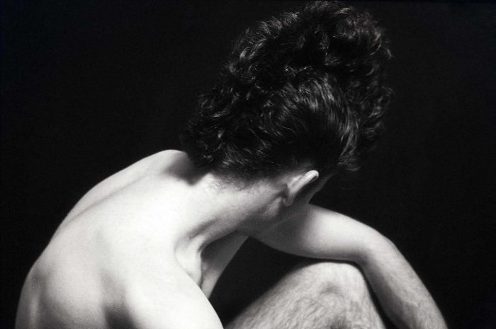 Black-and-white fine art portrait by Milan Stamenovic depicting a seated male figure in a withdrawn posture, exploring bodily resonance, inner rhythm, and the emergence of sonic identity before articulation.