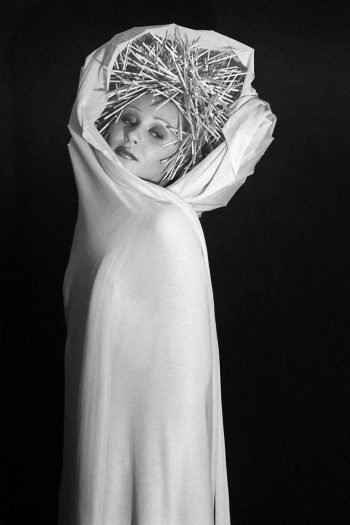 Black-and-white portrait photograph by Milan Stamenovic showing a draped figure crowned with a rigid, spiked structure, embodying the gradual collapse of performed identity, vulnerability beneath imposed roles, and the erosion of authenticity in contemporary portraiture (2004–2005).
