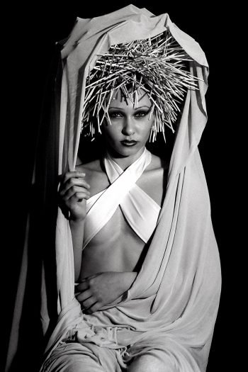 Black-and-white portrait photograph by Milan Stamenovic depicting a figure draped in white fabric and crowned with a rigid, spiked headdress, examining the burden of imposed roles, scripted identity, and the erosion of authenticity within contemporary portrait photography (2004–2005).