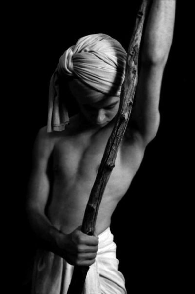 Black-and-white fine art analog portrait of a male figure holding a staff in contemplative stillness, exploring myth, restraint, and interior strength in photography by Milan Stamenovic.