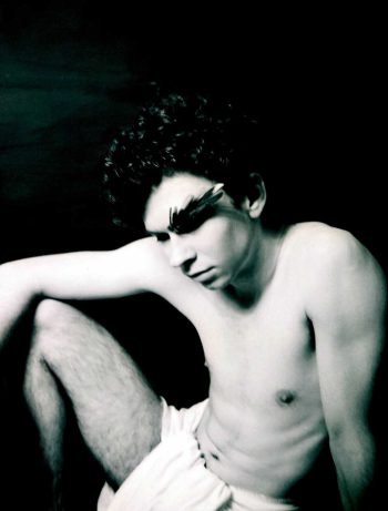 Black-and-white fine art analog portrait of a seated human figure in repose, expressing pause, vulnerability, and endurance within a myth-inspired photographic series by Milan Stamenovic.
