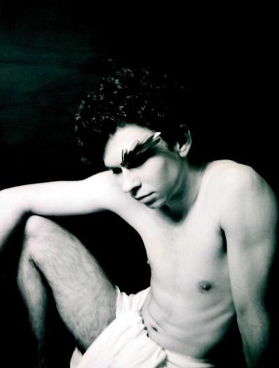 Black-and-white fine art analog portrait of a seated human figure in repose, expressing pause, vulnerability, and endurance within a myth-inspired photographic series by Milan Stamenovic.