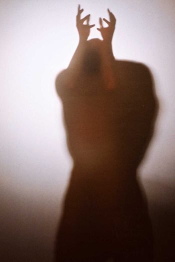 Portrait photograph of a blurred human figure with raised hands emerging through translucent surface, exploring instinct, identity, and pre-linguistic embodiment in Milan Stamenovic’s The Hidden Surface series.