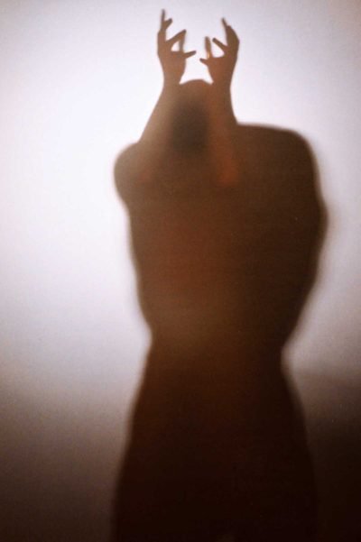 Portrait photograph of a blurred human figure with raised hands emerging through translucent surface, exploring instinct, identity, and pre-linguistic embodiment in Milan Stamenovic’s The Hidden Surface series.