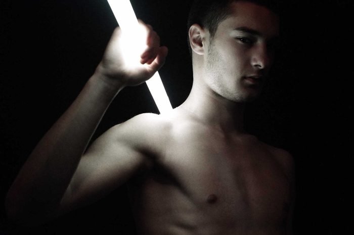 Portrait photograph examining the physical consequence of artificial illumination on the human body, isolating light as an active force rather than a neutral source.